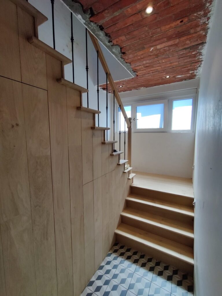 Landelijke trap in Engelse stijl tijdens plaatsing in Kalmthout, zicht op de deur onder de trap, en de treden die over de trapwang komen, ook met zicht op het bordes